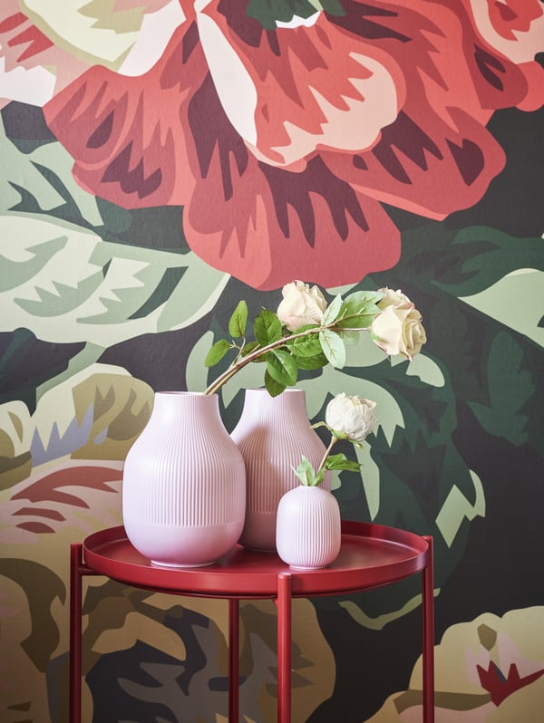 GRADVIS vases on a red side table in front of the bold floral wallpaper in the background.