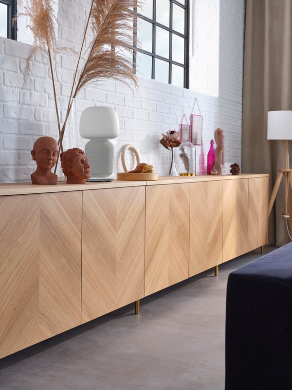 Kombinasi storan berpintu BESTÅ venir kayu oak terletak bersandar pada dinding batu bata berwarna putih, lampu lantai kayu ash/berwarna putih, objek-objek hiasan.