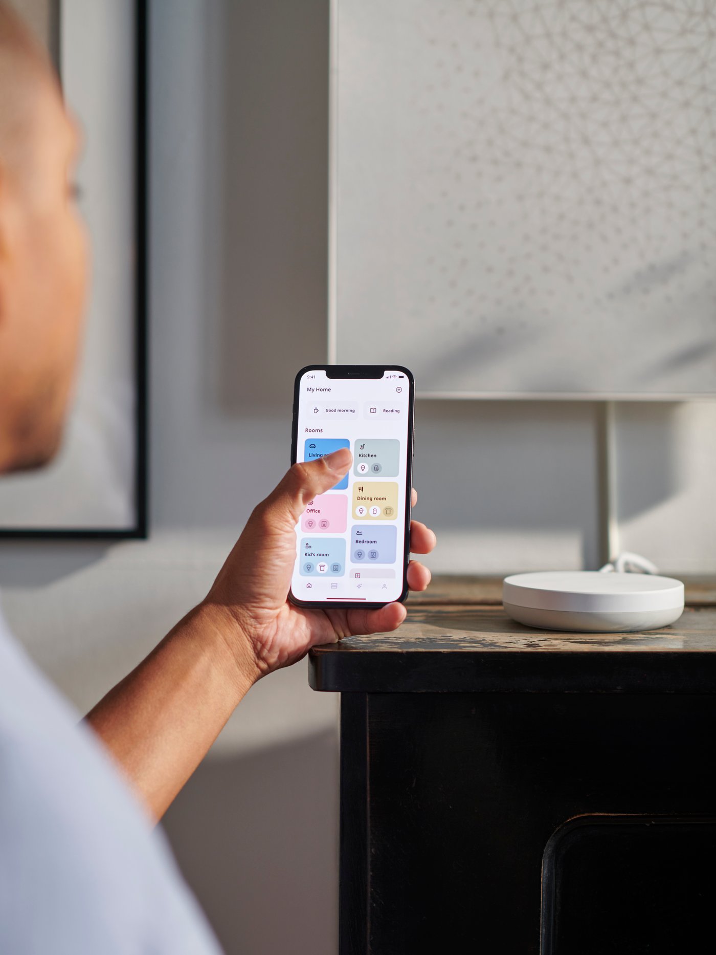 A persons holds the IKEA Home smart app open next to a DIRIGERA Home smart hub.