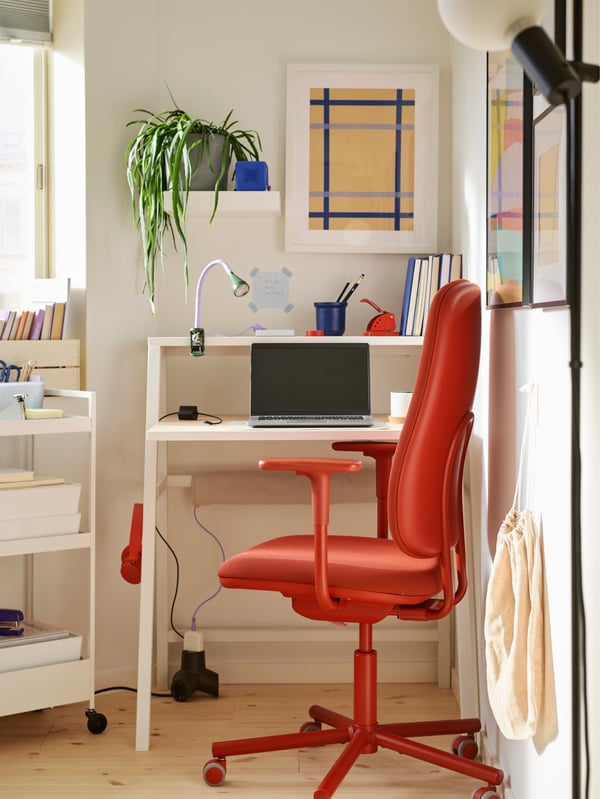 A small corner workspace with a MITTPLAN desk, a red SMÖRKULL office chair, a laptop, and a white trolley with storage boxes.