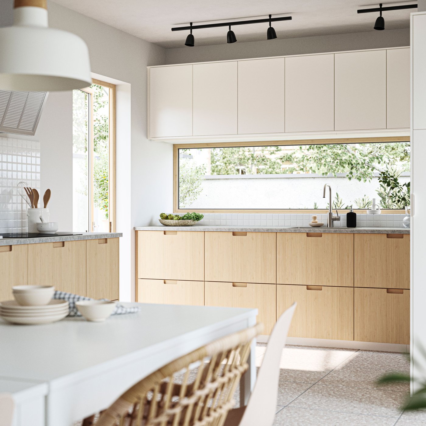 A kitchen and dining area with windows facing a garden. FRÖJERED fronts, in bamboo, are combined with VEDDINGE fronts in white.
