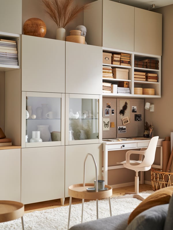 Warmly lit living room featuring the BESTÅ storage combination, white stain HEMNES desk with two drawers and a swivel chair.