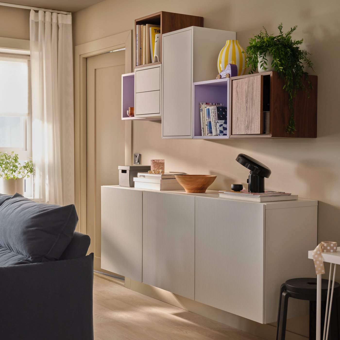 A softly sunlit living room with an asymmetric combination of EKET and BESTÅ wall cabinets, holding books and decoration.