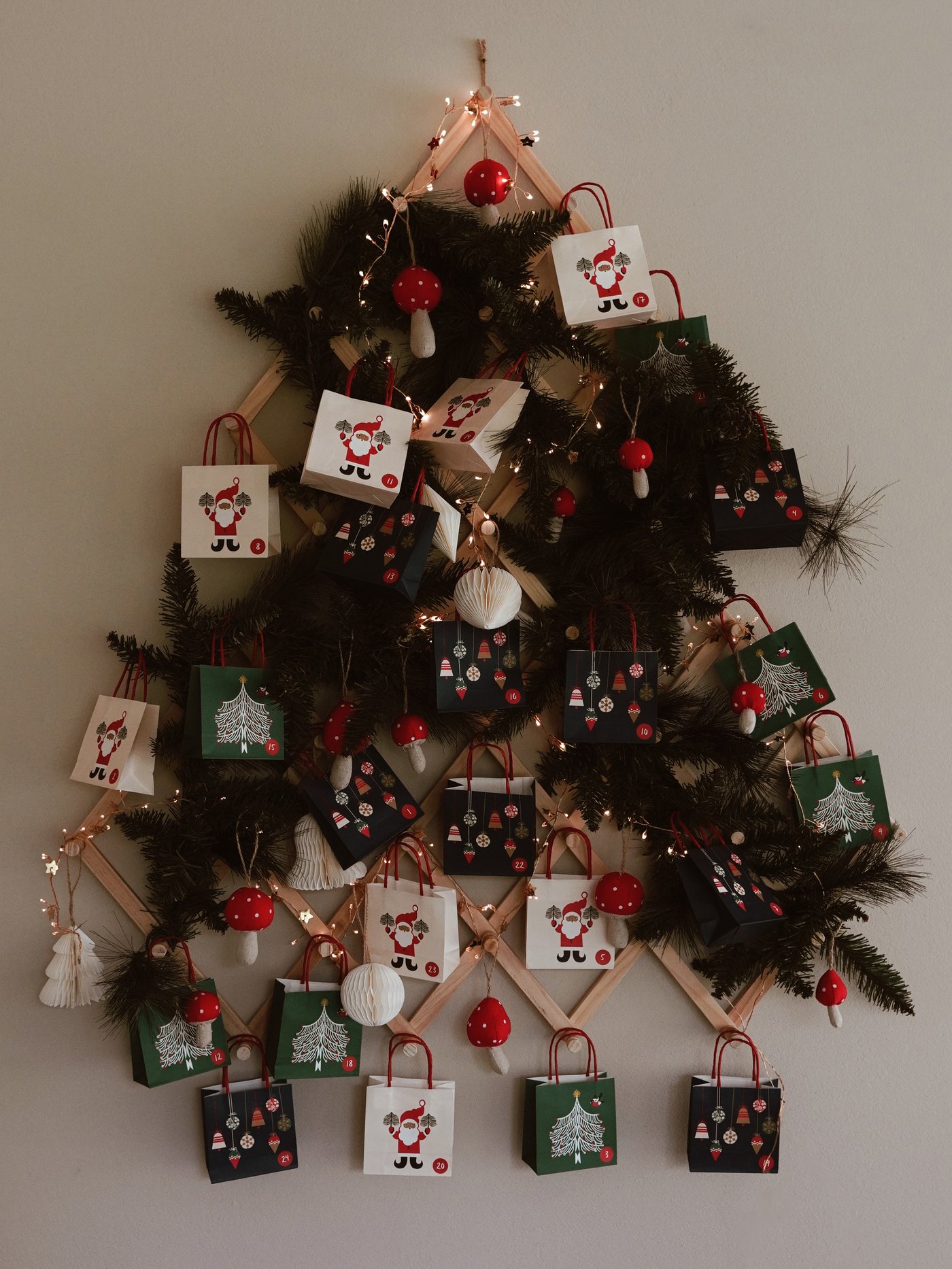 Wandmontierter Weihnachtsbaum aus Zweigen, geschmückt mit festlichen Papiertüten, Tannenzapfen und Lichtern, der eine warme Weihnachtsstimmung verbreitet.