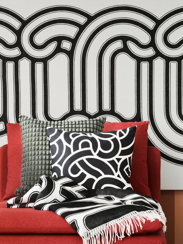 A mustard coloured sofa with red and pink cushions sits next to a black and white striped rug. Red artwork hangs on the wall.