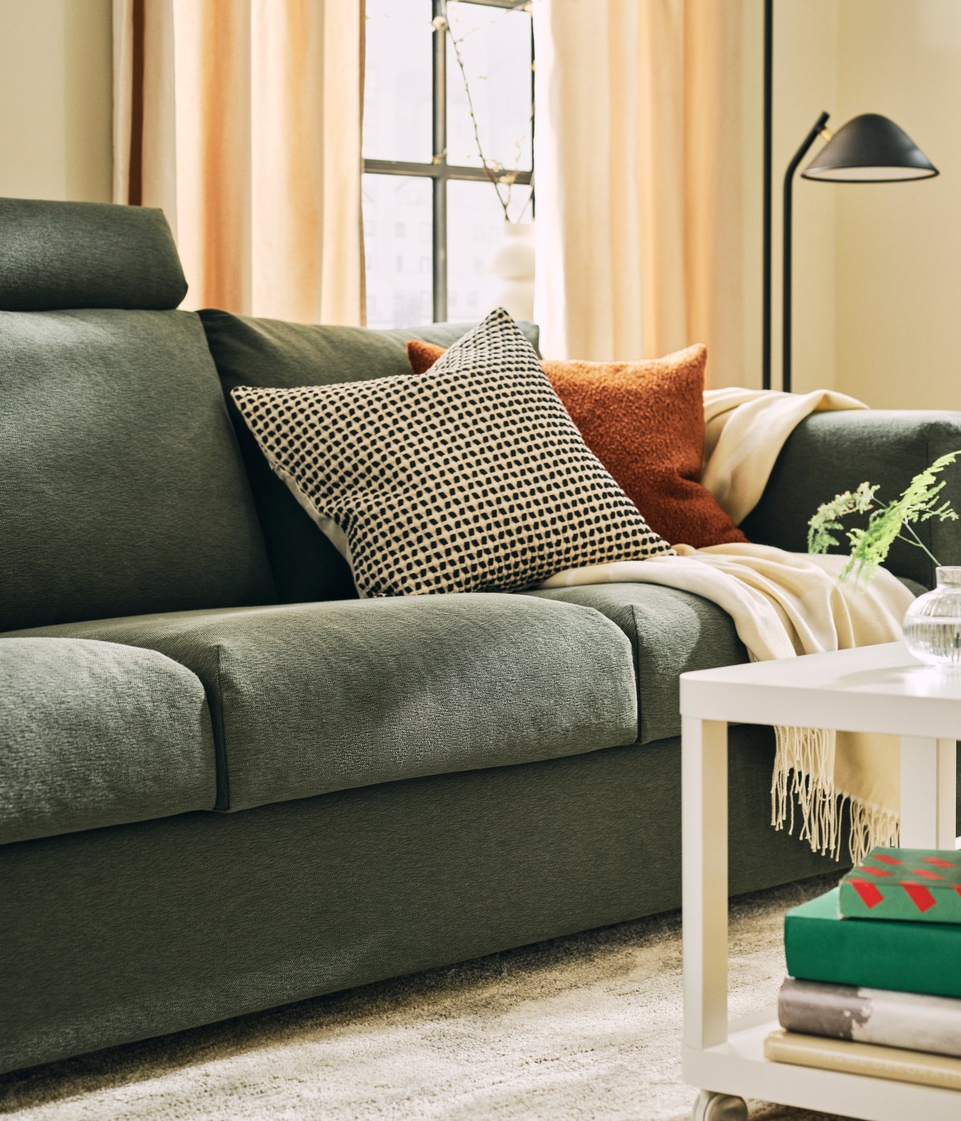 Part of a light living room with a grey-green VIMLE three-seat sofa next to a white TINGBY side table and a floor lamp.