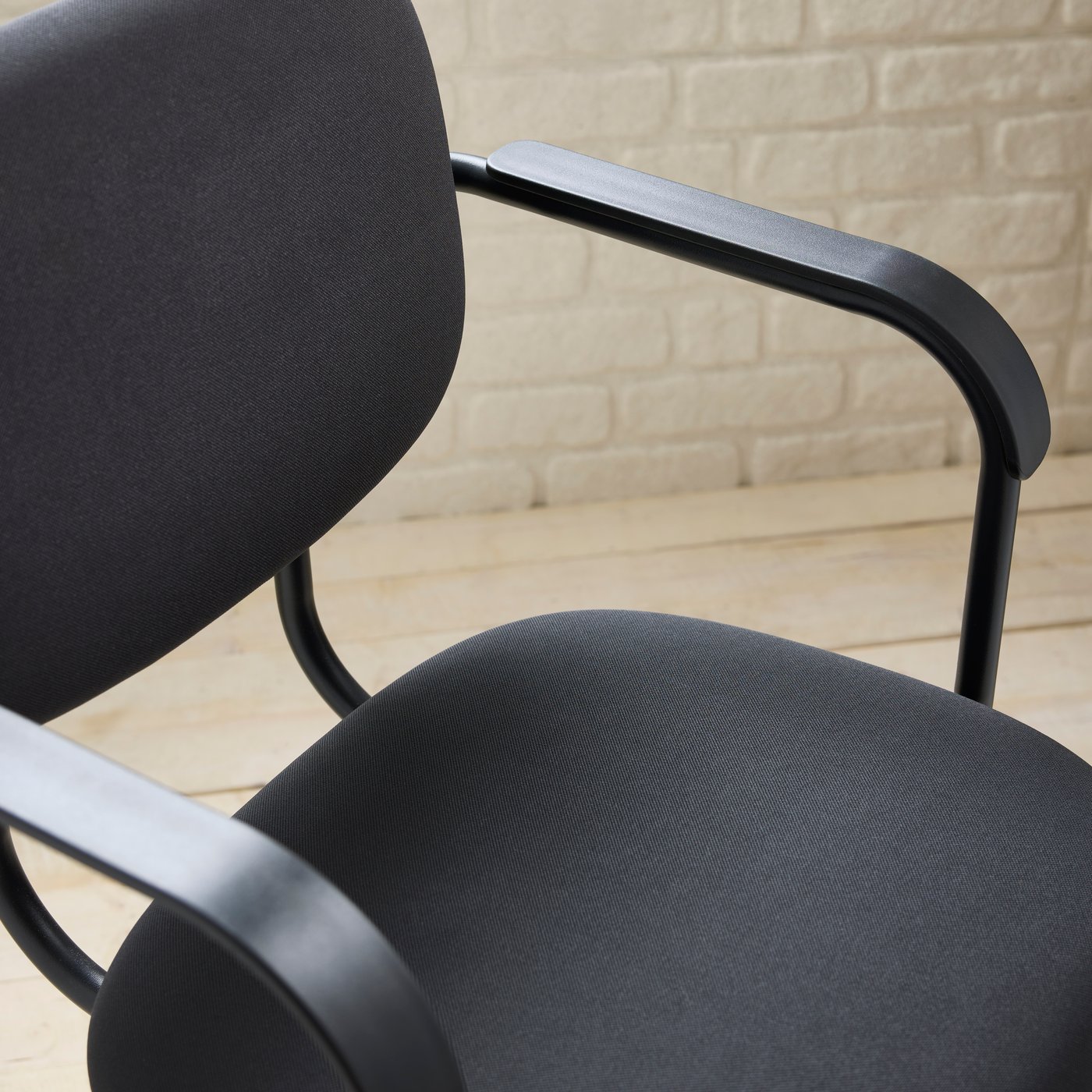 A close-up of a dark grey MULLSJÖ swivel chair against a white brick wall, standing on a wooden floor.