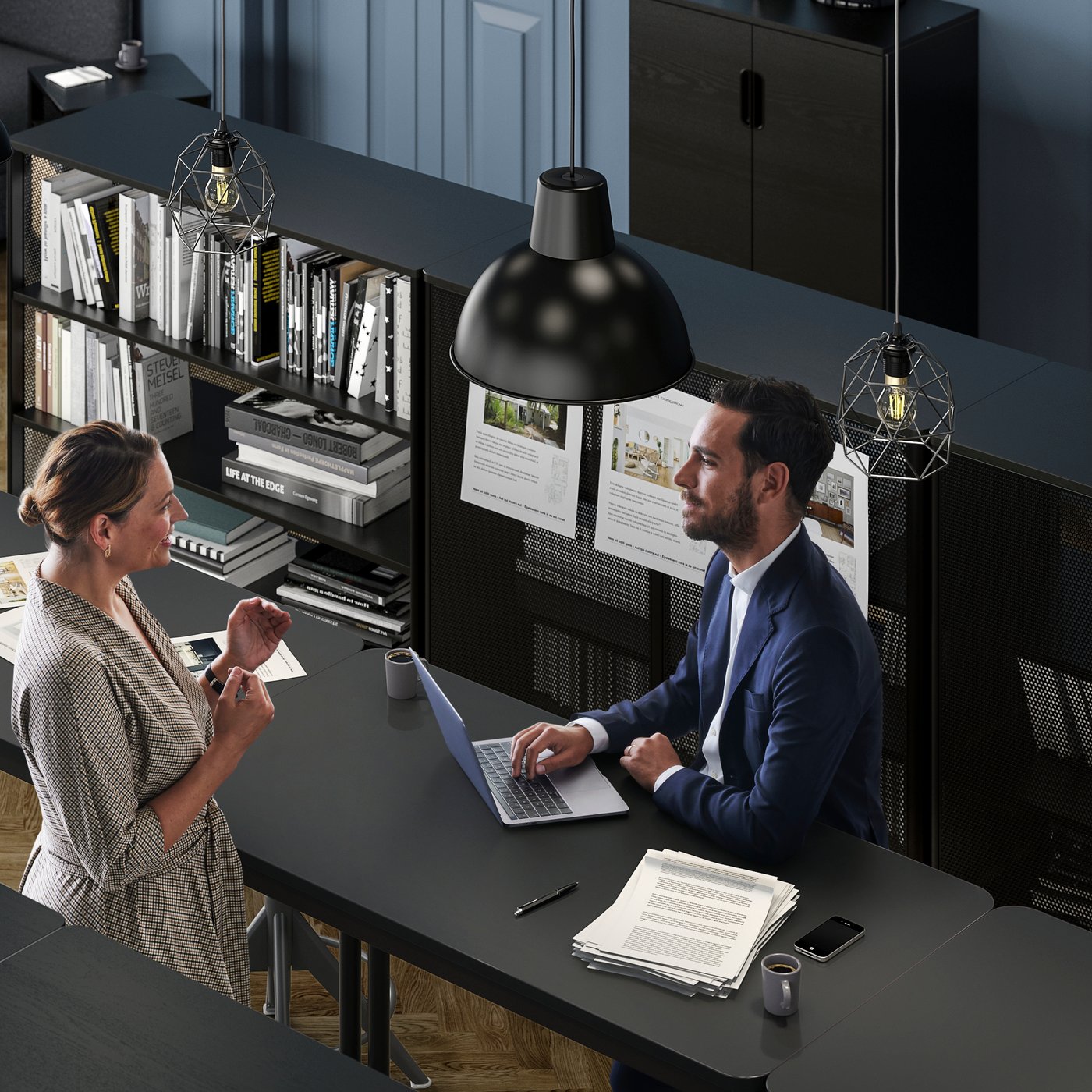 An office setting where a woman talks to a man in a suit who sits with his laptop by a TOMMARYD table.