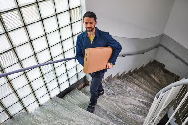 An IKEA delivery man carrying a parcel walking up a flight of stairs.