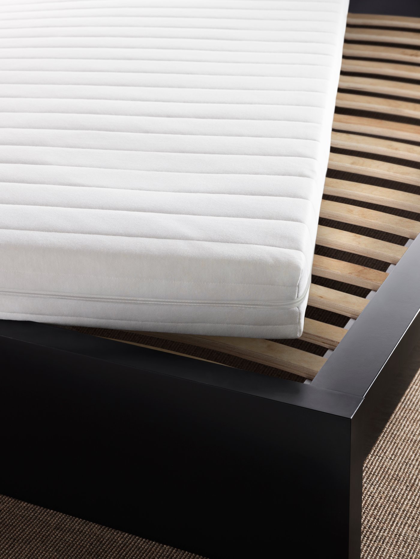A bed with a black-brown frame and a white mattress at an angle on top to reveal a LURÖY slatted bed base.