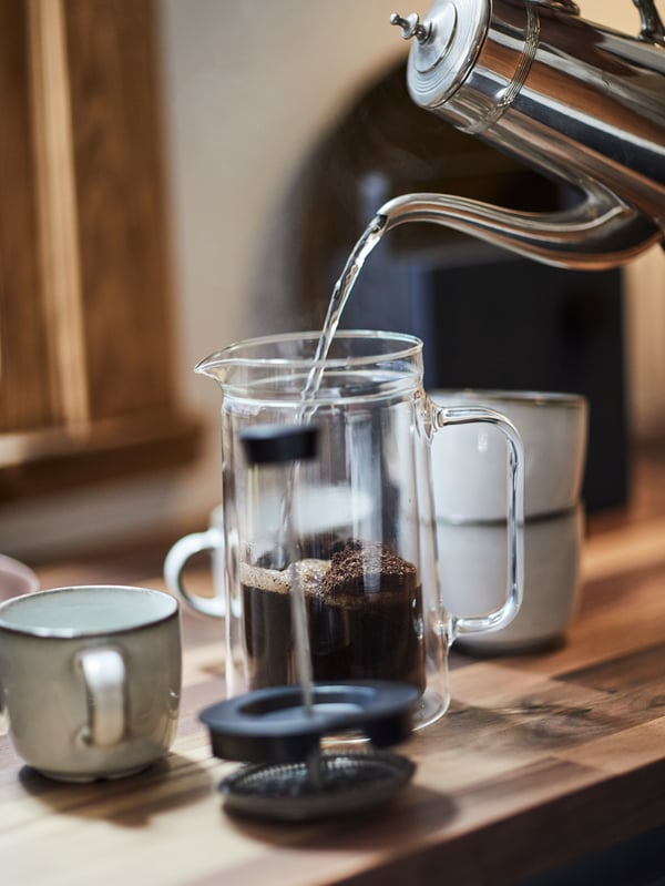Water being poured from a silver kettle into an EGENTLIG coffee maker on a wooden worktop.