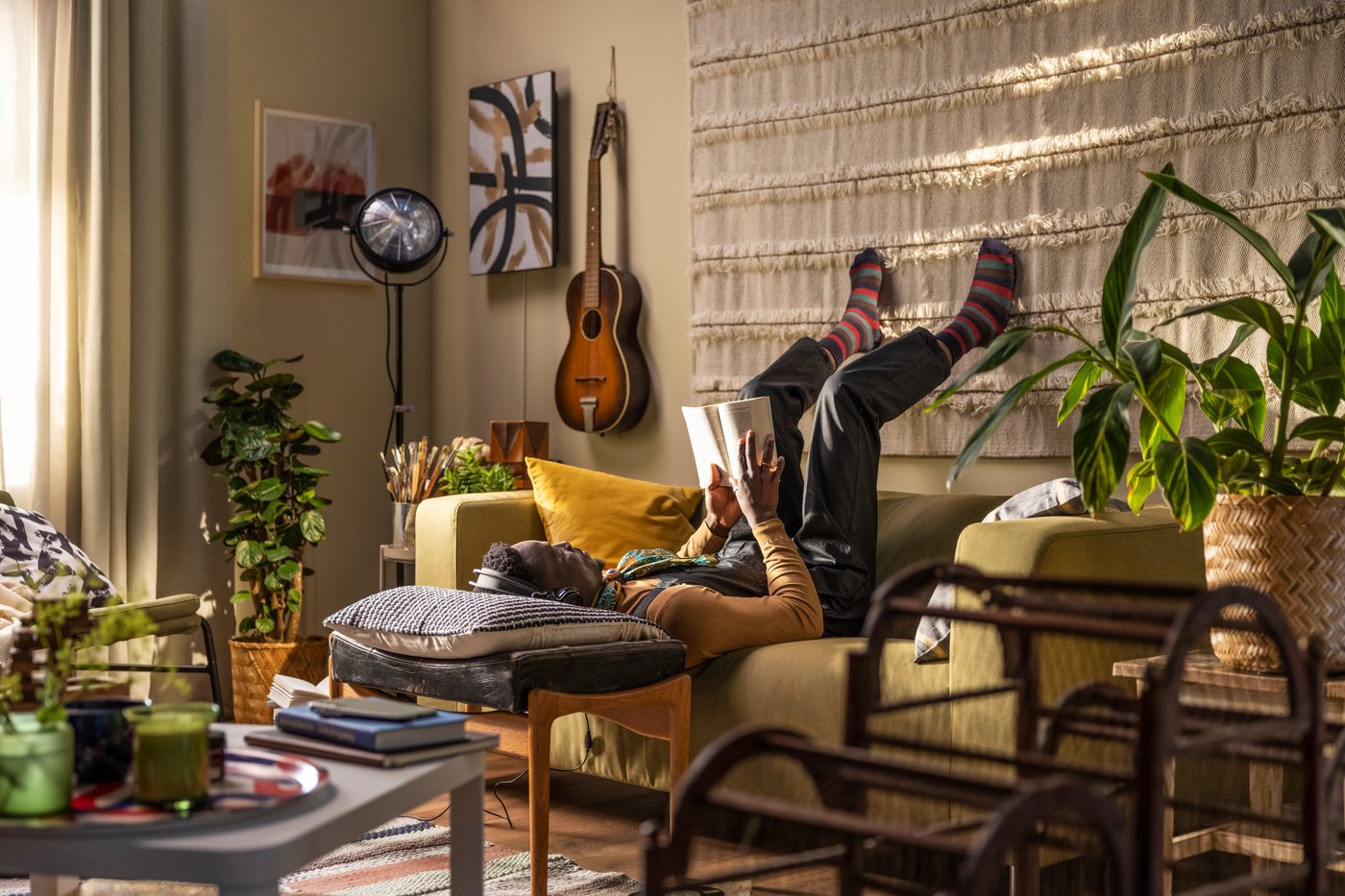 A person laying on a yellow sofa upside down and reading a book, his head on a pillow resting on a coffee table.