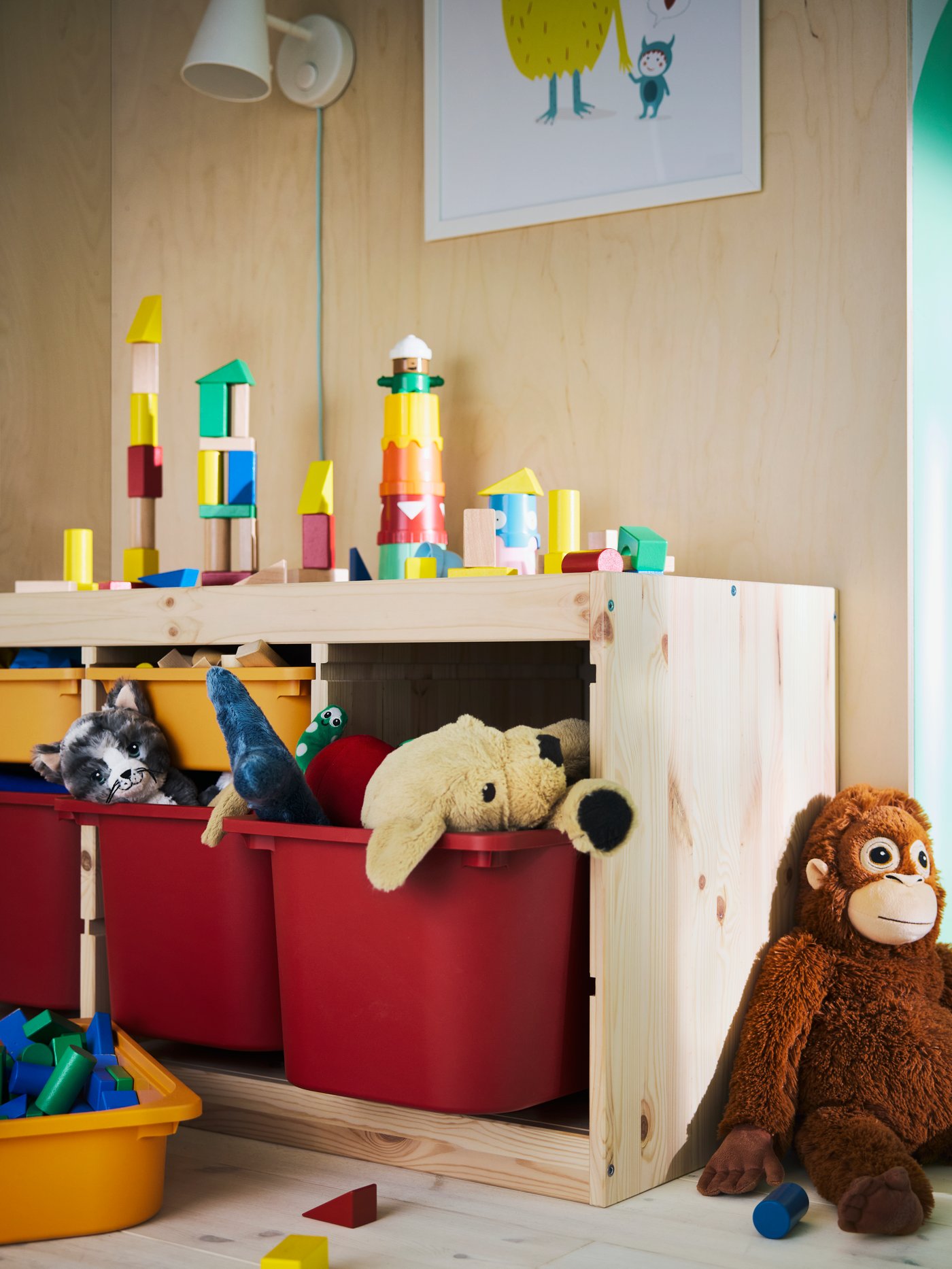 TROFAST storage unit with lots of toys both on top and in red/orange plastic boxes. A soft toy monkey leaning against it.