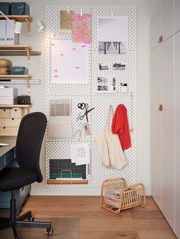 A wall with white pegboards, a year planner, black and white photographs, scissors, a tote bag.