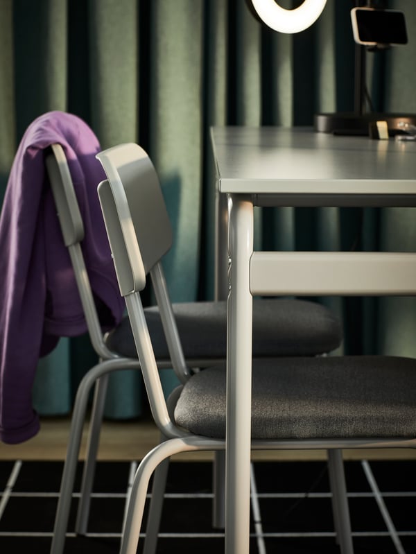The side of a grey GRÅSALA table and two grey GRÅSALA chairs with a dark green curtain in the background.