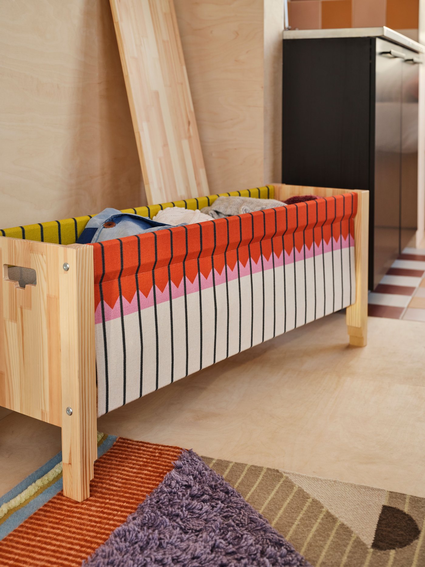 An OMMJÄNGE bench with storage with various items stored inside sits by a wall, with the lid of the bench resting beside it.