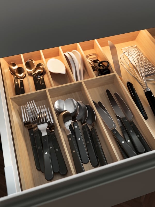 An open drawer with UPPDATERA drawer organisers in light bamboo holding knives, forks, spoons and various other items.