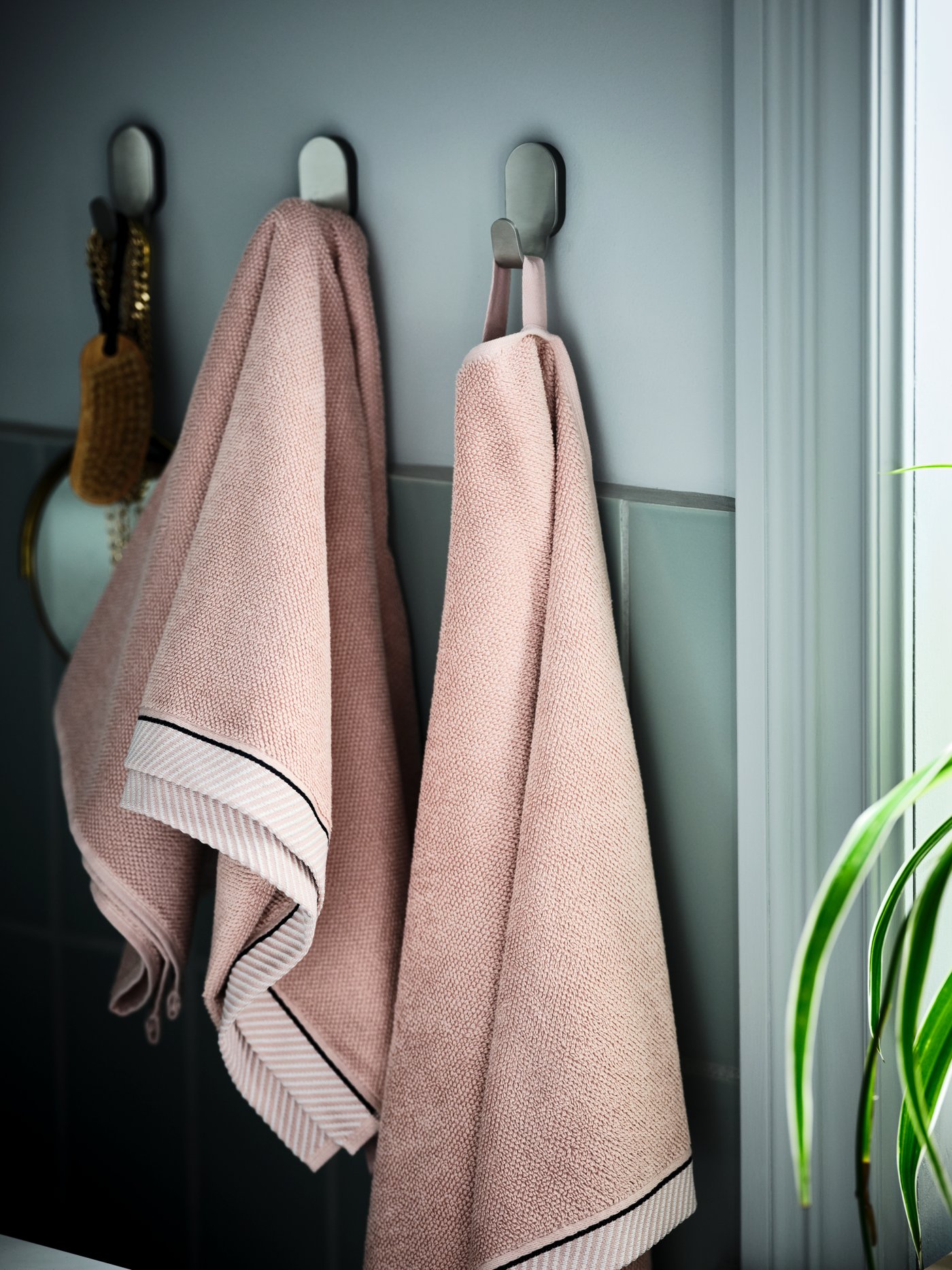 Zoom a una pared de baño con colgadores de toallas sosteniendo dos toallas color rosa.