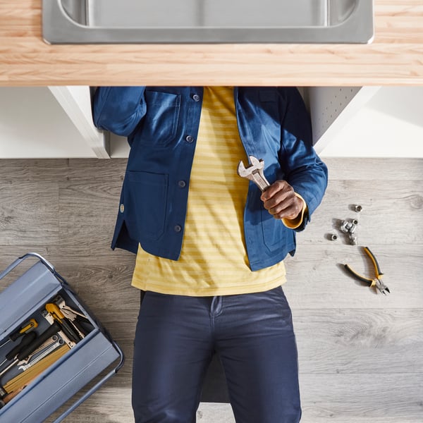 Man in the cabinet under the sink with plumbing wrench in hand