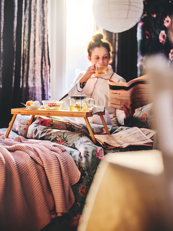 Una mujer comiendo desayuno sobre la cama con una bandeja RESGODS.