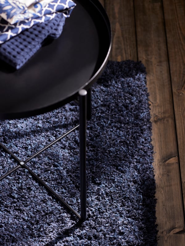 Blue patterned bedroom textiles on a black GLADOM tray table on a dark blue rug.
