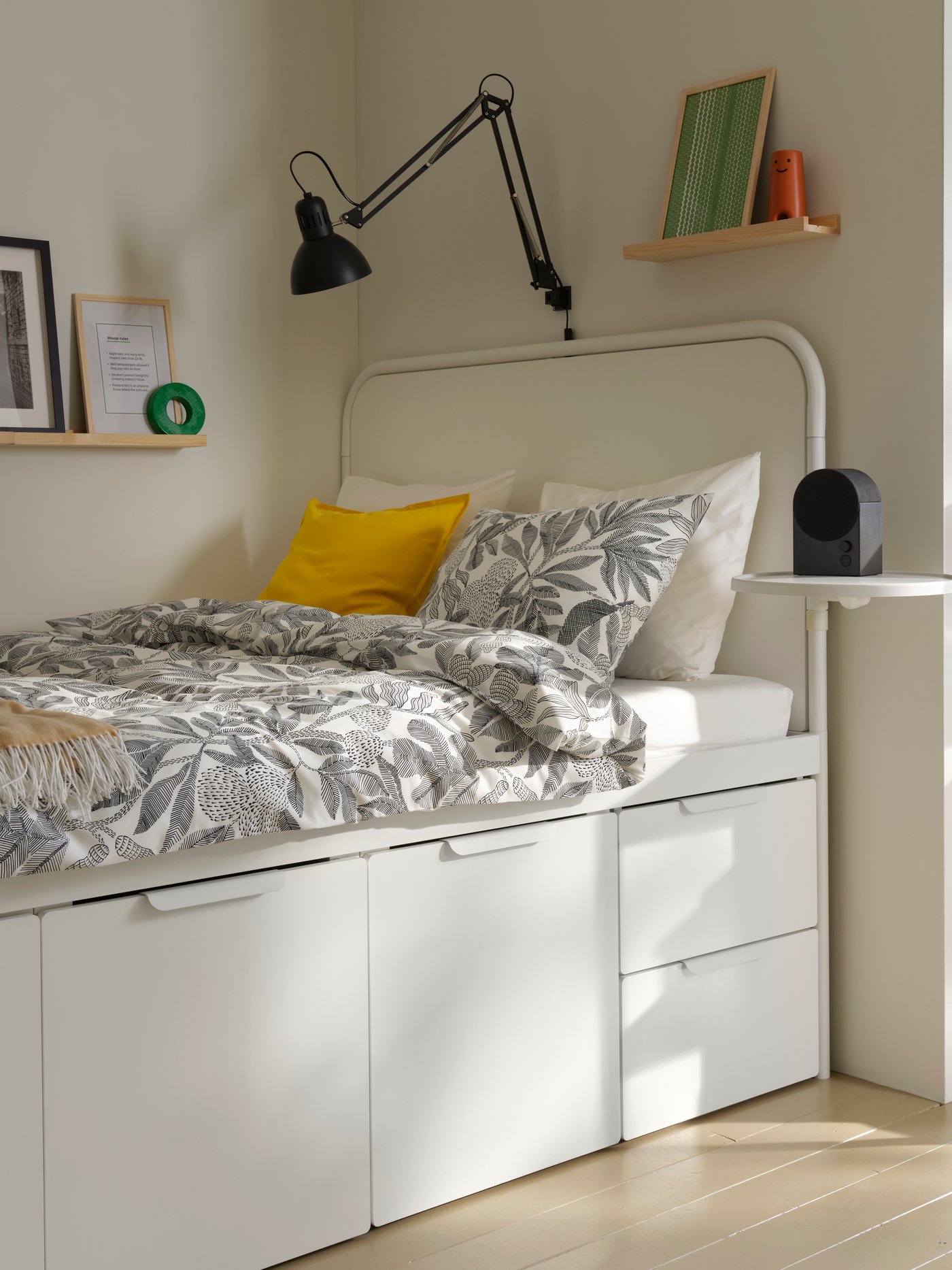Blick auf ein weisses MÅSSKÄR Bettgestell mit Stauraum in einem Studentenwohnheim. Auf dem Bett liegt eine schwarz-weisse Bettdecke mit Blumenmuster.
