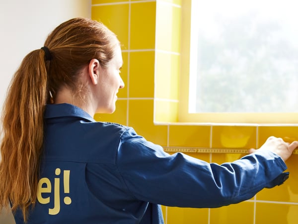 En IKEA-medarbejder i blå jakke måler en væg ved siden af ​​et vindue.