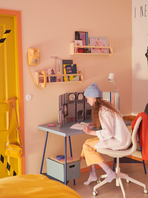 A pastel room where a girl sits at a study space formed by a blue LAGKAPTEN/TILLSLAG desk and a LÅNGFJÄLL office chair.