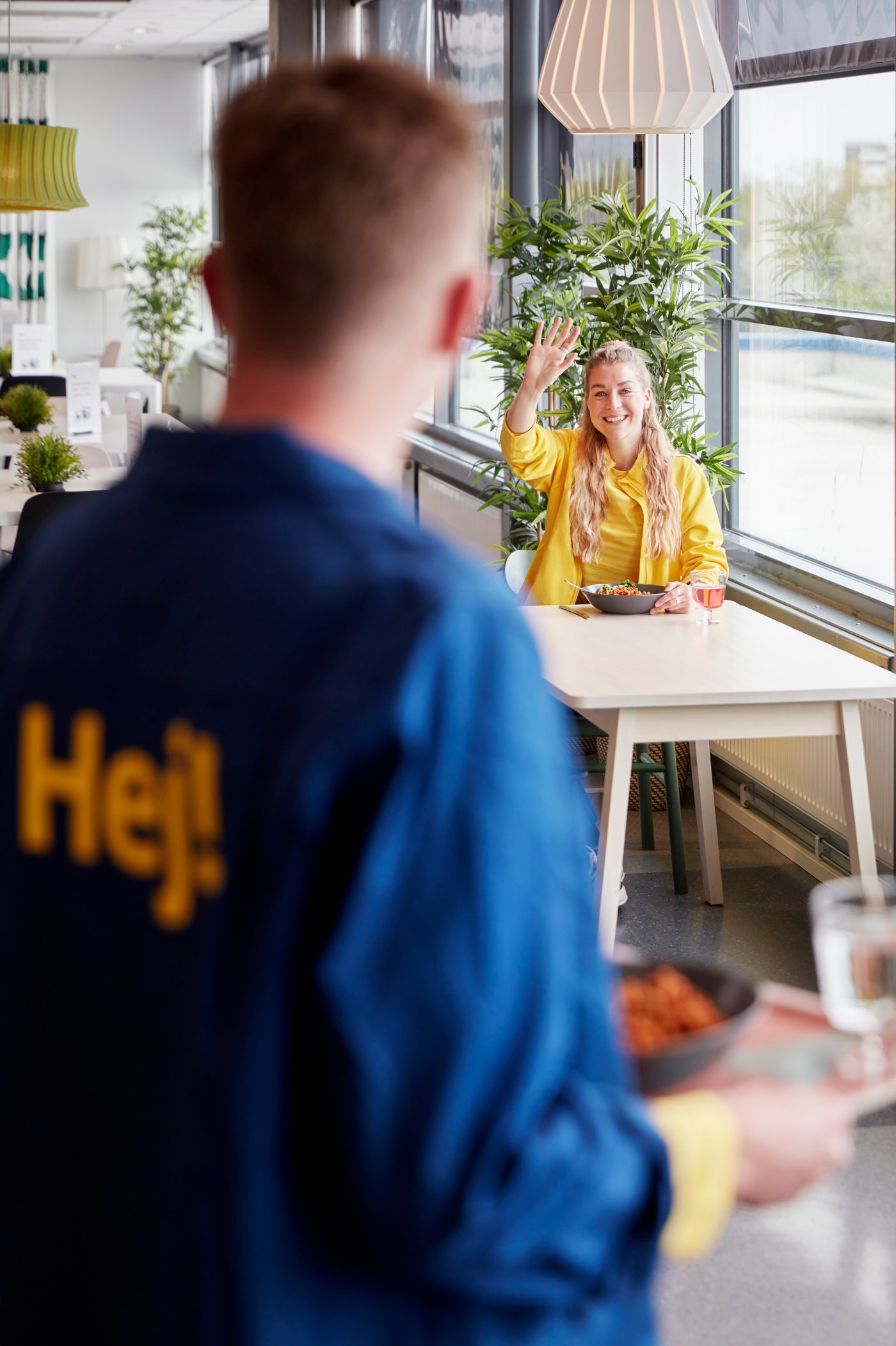 En smilende IKEA medarbejder inviterer en kollega til at spise frokost sammen i kantinen.