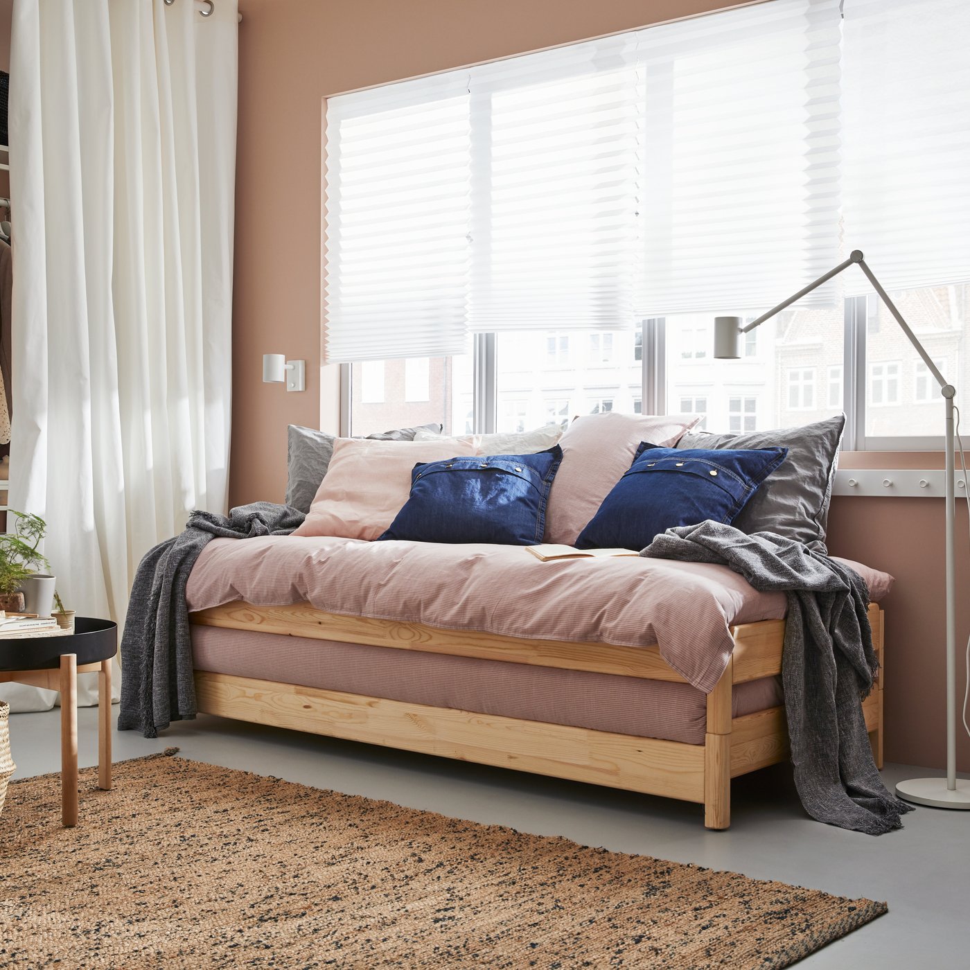 A stackable UTÄKER bed sits up against a wall with a window in a bedroom.