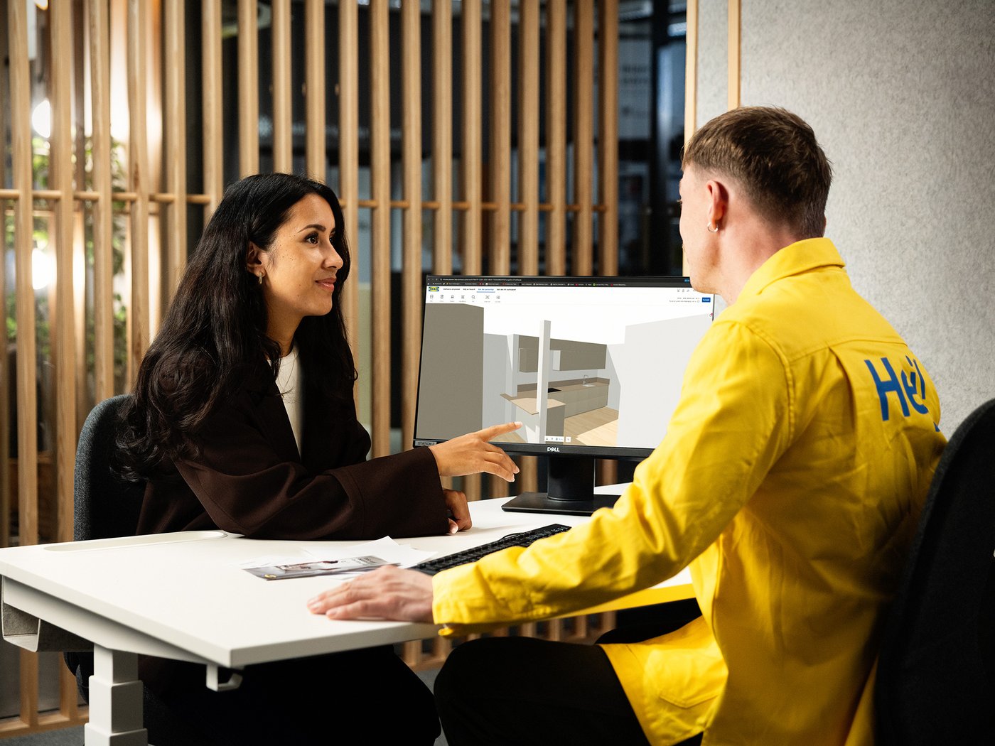 Två personer sitter vid ett skrivbord och diskuterar en digital köksplan på en datorskärm.