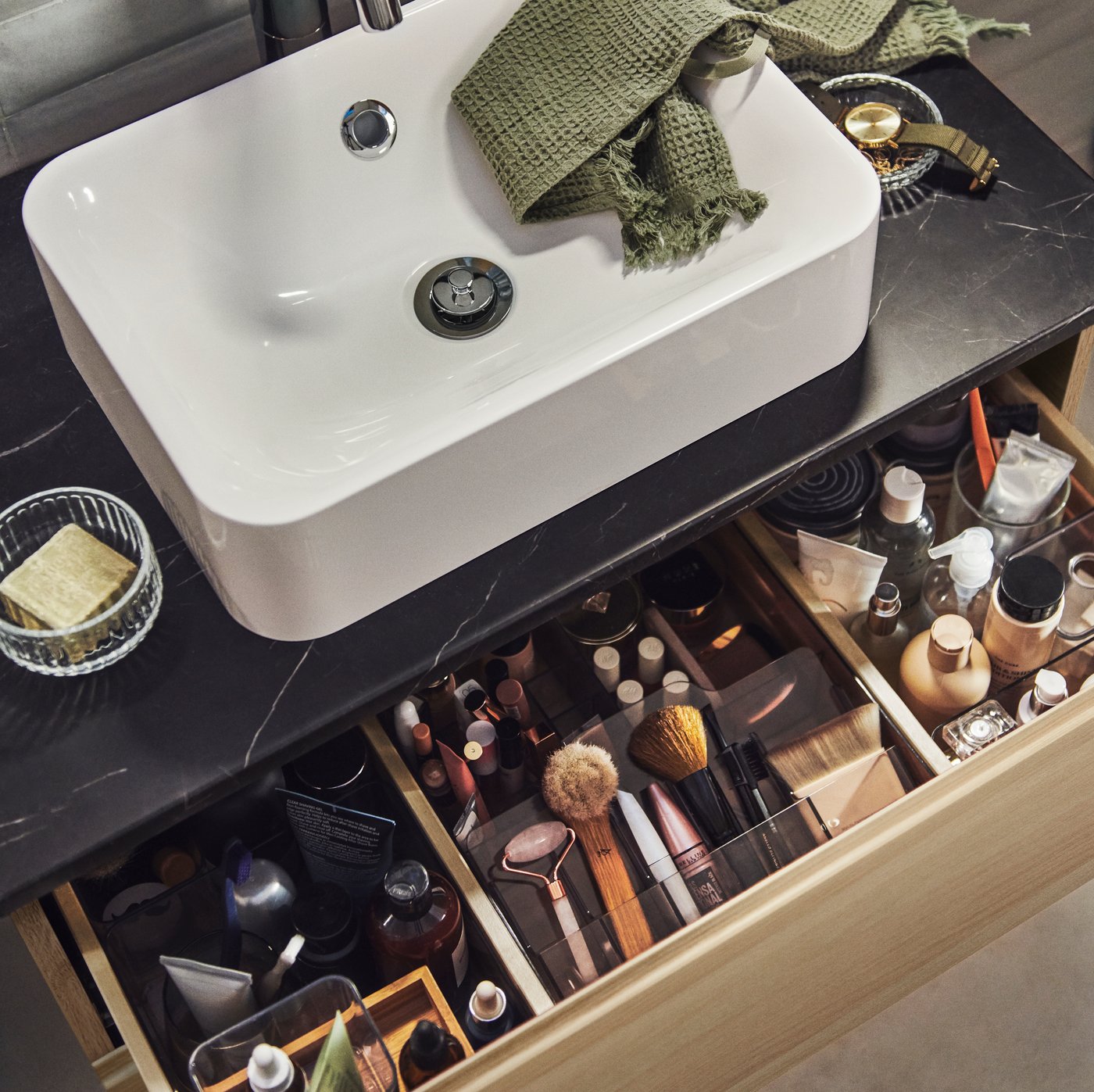 Es ist ein HÖRVIK Aufsatzwaschbecken auf einem Waschbeckenschrank zu sehen, an dem eine Schublade ausgezogen ist. In der Schublade sind Make-up und organisierte Accessoires zu erkennen.