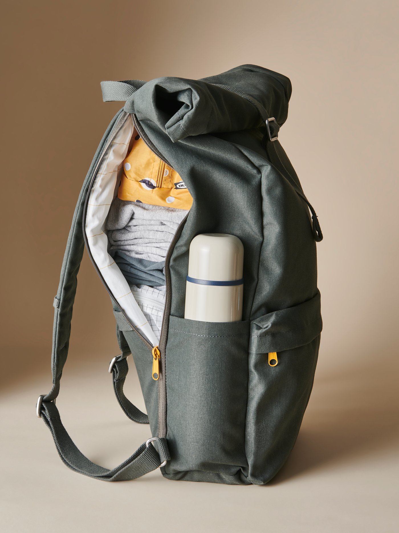 Un sac à dos vert DRÖMSÄCK dézippé d’un côté, transportant des vêtements, des sacs RENSARE et une bouteille isotherme HÄLSA.
