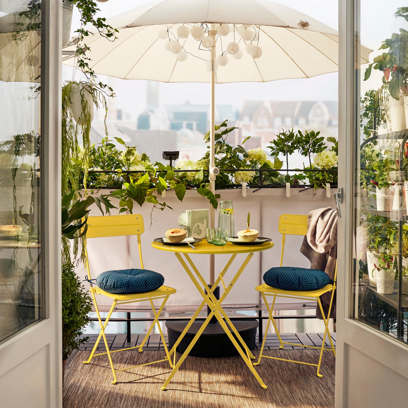 IKEA SUNDSÖ yellow table with 2 chairs on a balcony with IKEA HÖGÖN parasol.