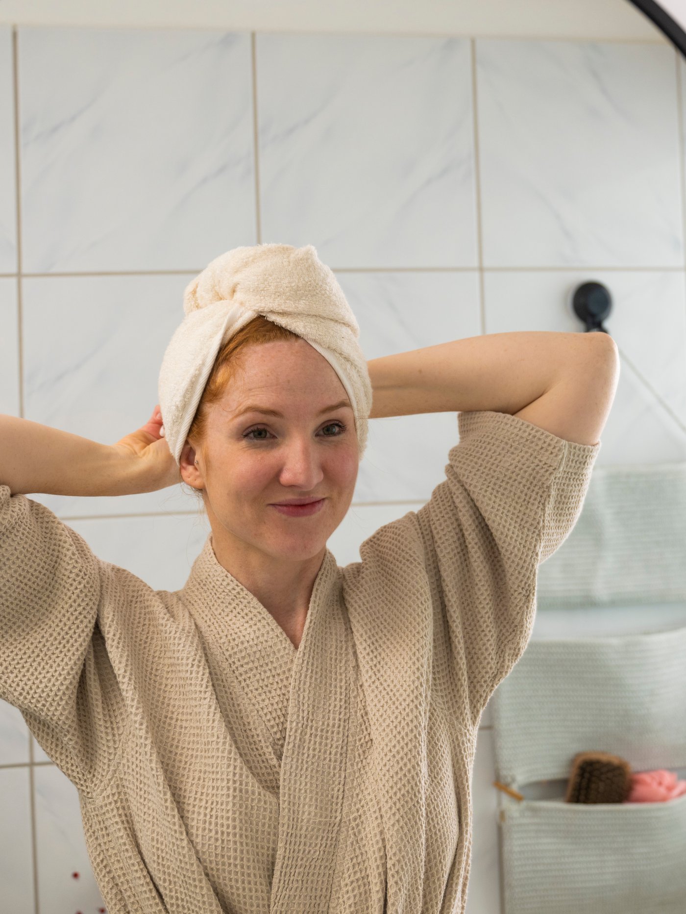 Žena stoji ispred ogledala i omotava peškir oko glave.