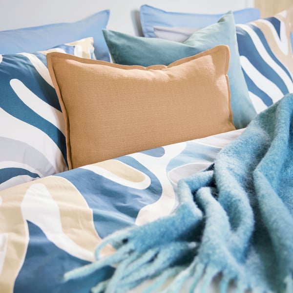Plano de cama com capa de edredão e fronhas MYGGLASVINGE com padrão de folhas realçadas por manta em turquesa acinzentado.