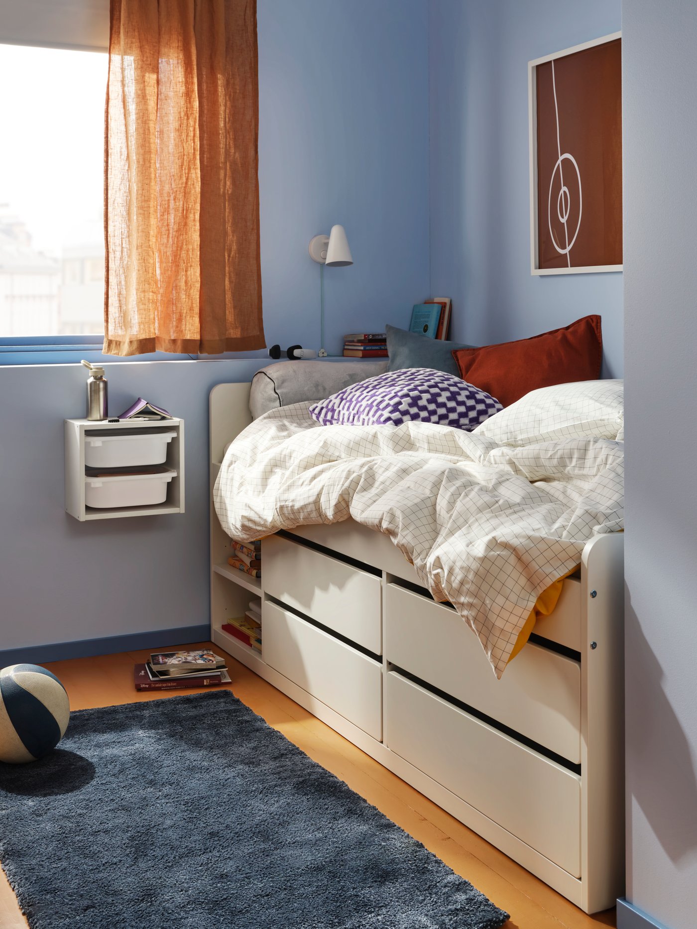 SLÄKT bed in the corner of a bedroom with light blue walls, a blue rug and a window in the back.