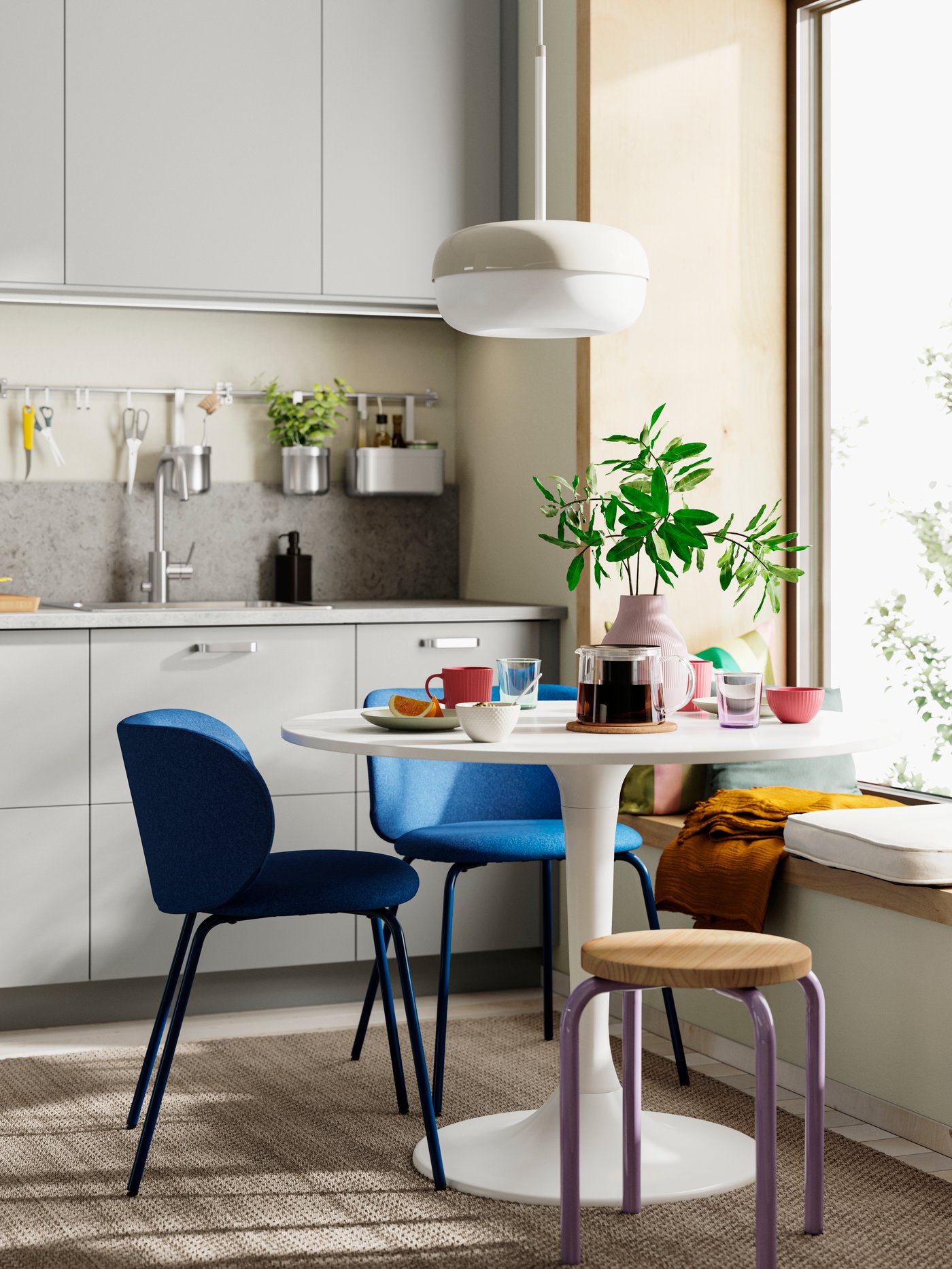 A kitchen with a DOCKSTA table with blue chairs, HAVSTORP light grey fronts, potted plants, and a window seat with cushions.
