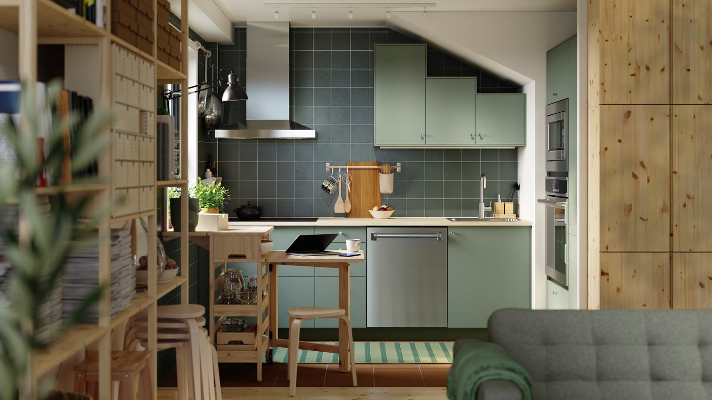 A green L-shaped kitchen has gray green NICKEBO fronts and a RESARÖ mobile drop-leaf table with storage and some stools.