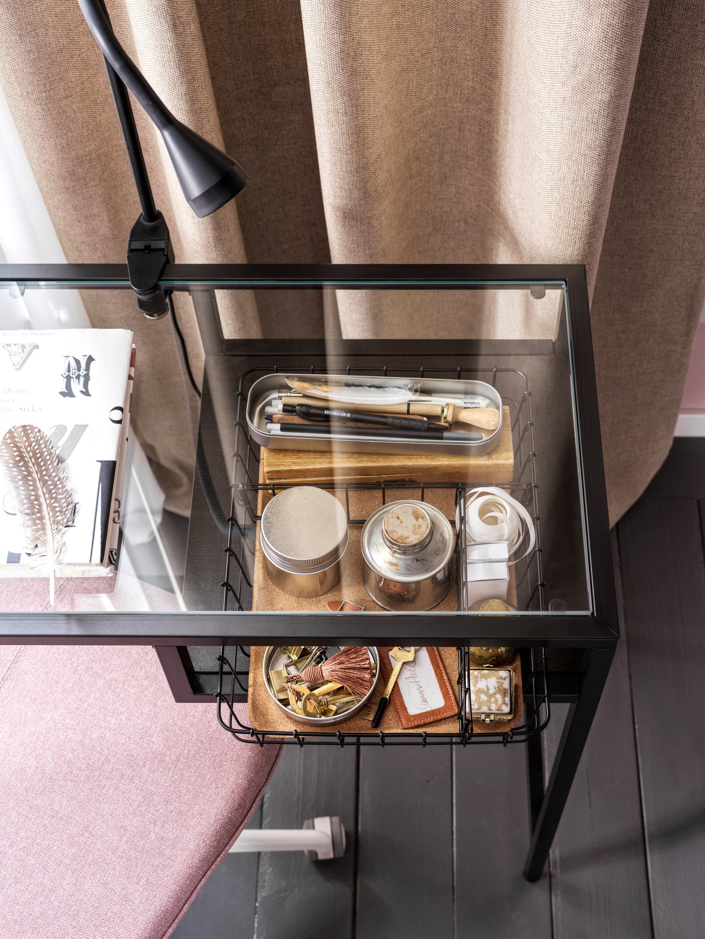 A VITTSJÖ laptop table with a glass top. Below the glass top is a tray with different accessories.