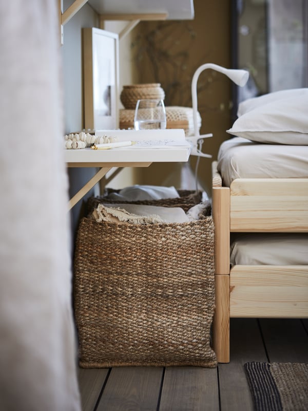 A shelf functioning as a bedside table, two TJILLEVIPS natural seagrass baskets and a white NÄVLINGE LED clamp spotlight.