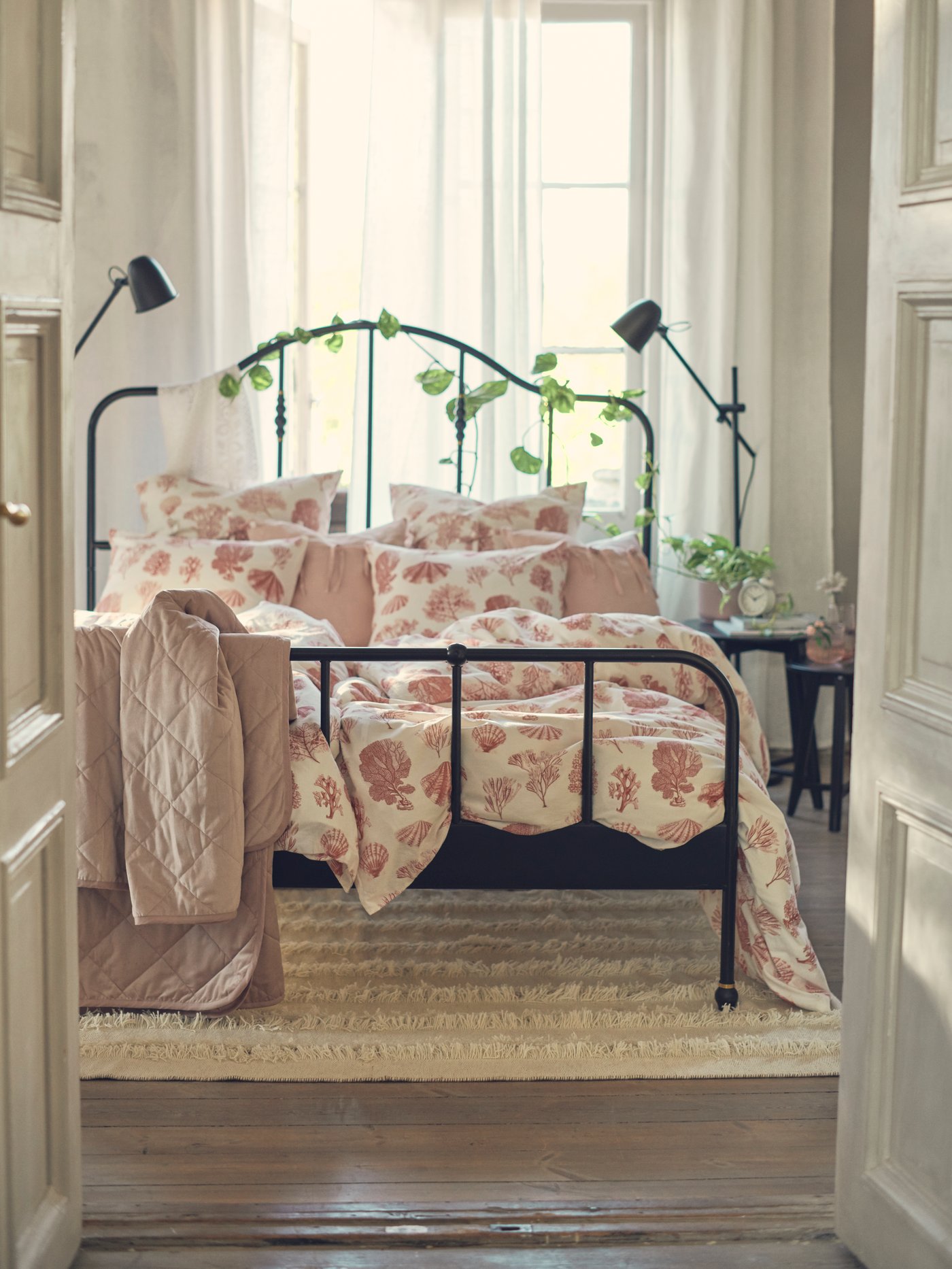 Una cama de fierro con ropa de cama rosada en una habitación matrimonial.