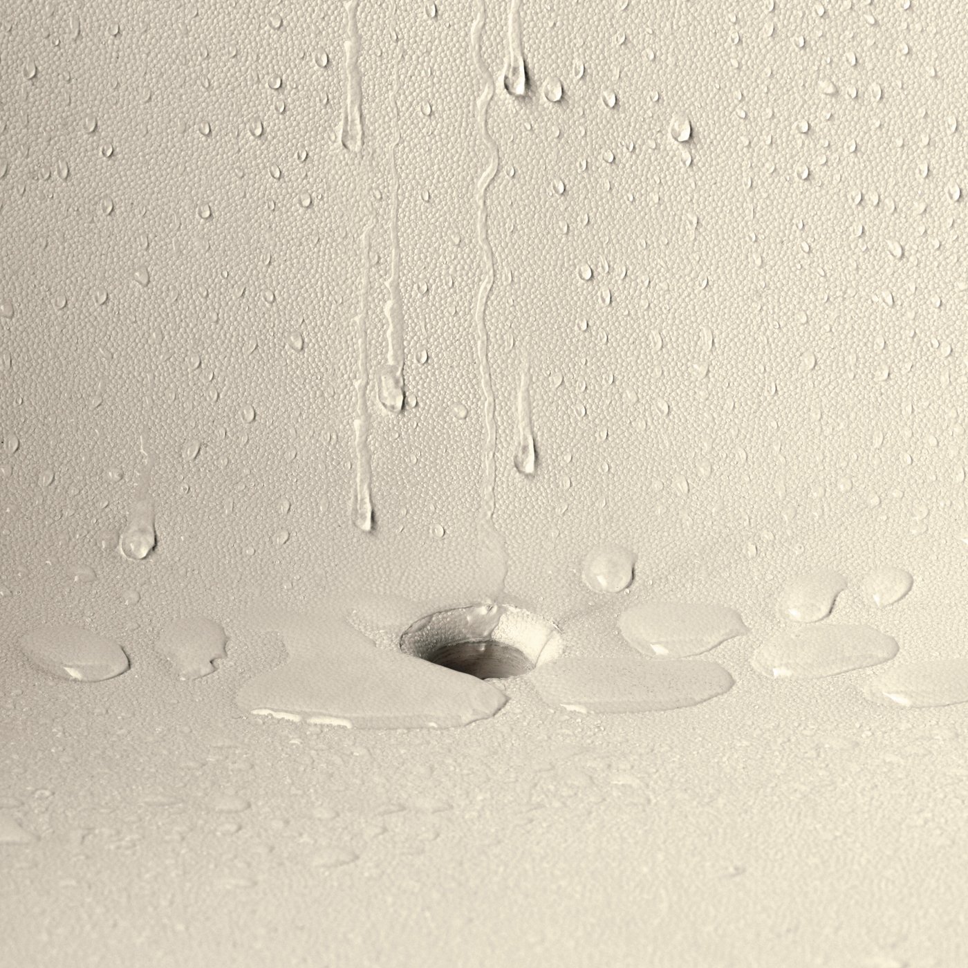 Vatten droppar ner på en plastyta och bildar droppspår och små vattensamlingar.