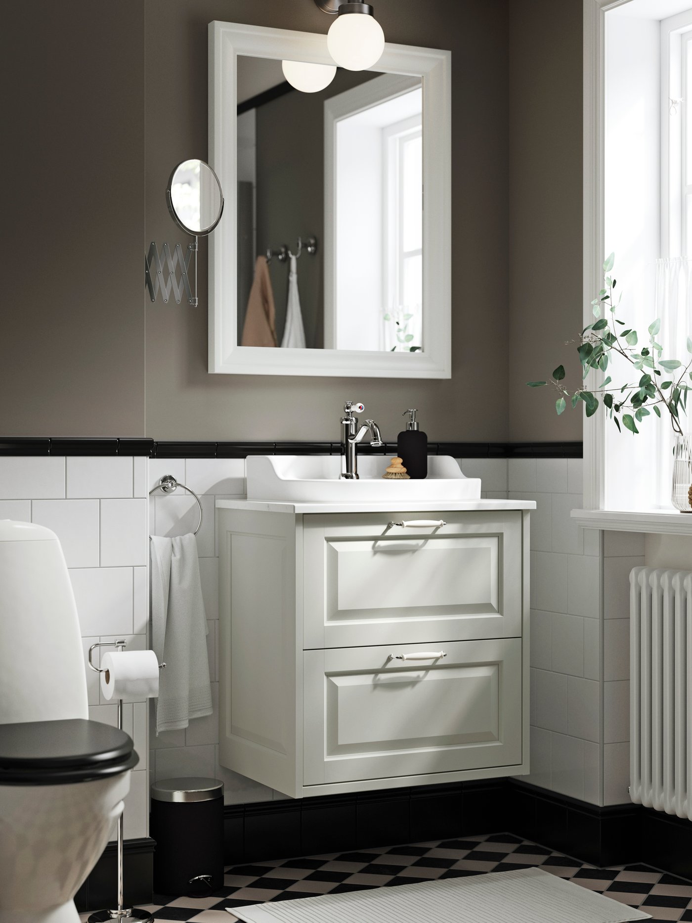 A white TÄNNFORSEN washstand with two drawers and white handles is placed on a white-tiled bathroom wall below a mirror.