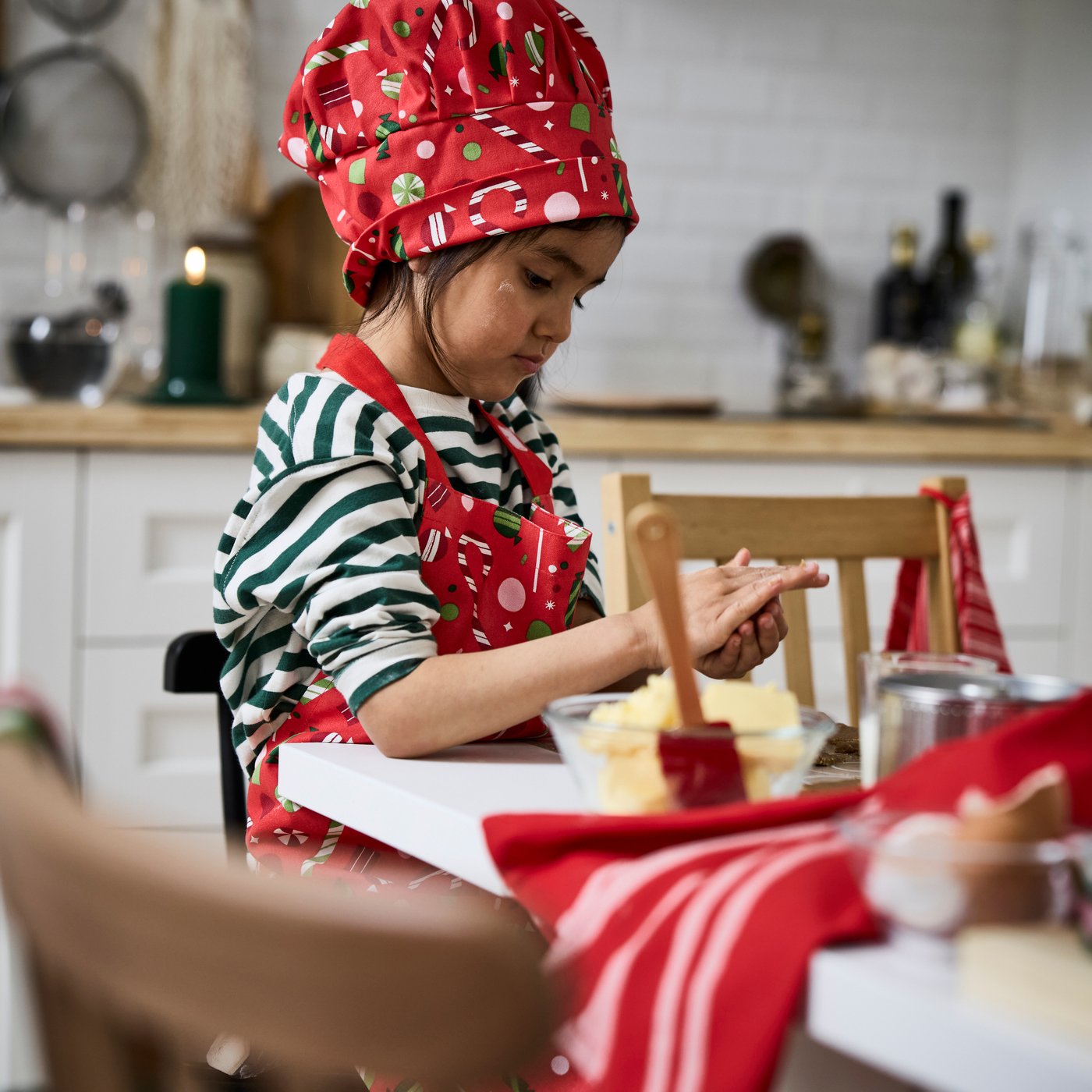 A child is wearing a red VINTERFINT children’s hat while rolling dough with their hands.