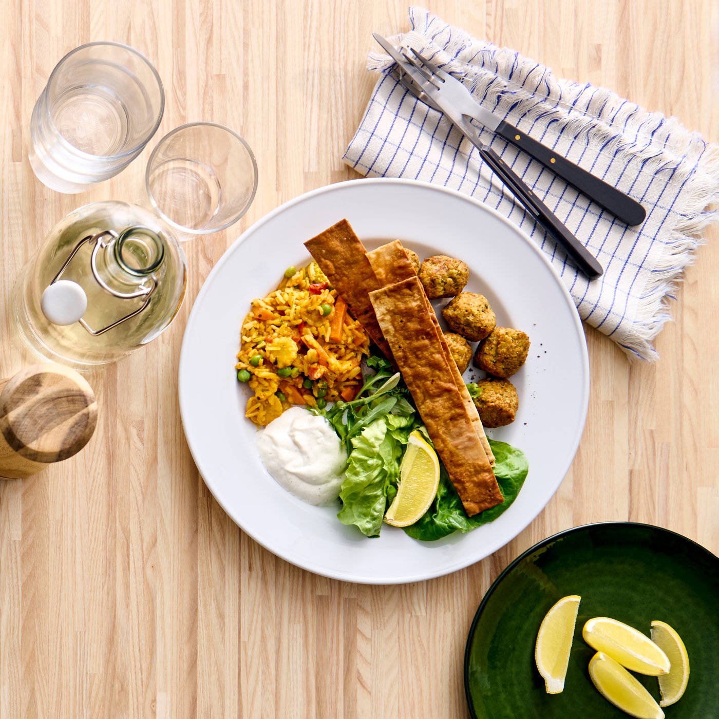Falafel con riso e verdure serviti in un piatto bianco su un tavolo da pranzo in betulla.