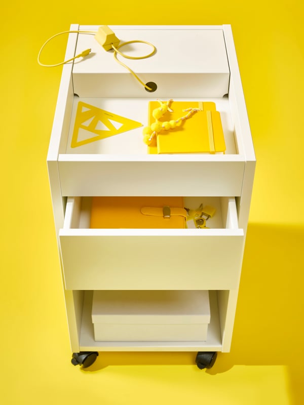 An open white TONSTAD drawer unit on castors filled with yellow office supplies against a bright yellow background.