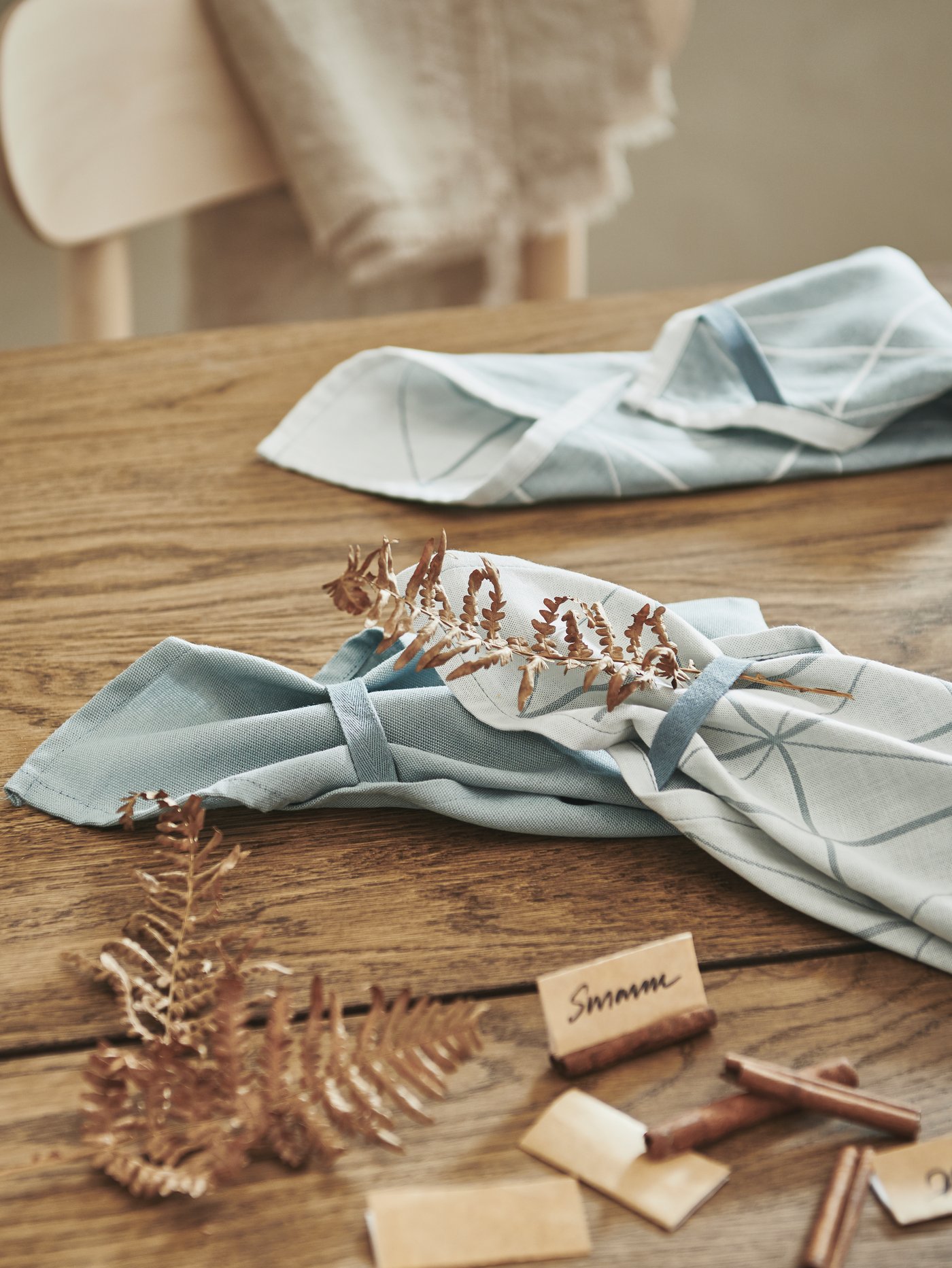 A wooden tabletop being prepped for a party, with decorations, handwritten name signs and folded, blue SANDVIVA tea towels.