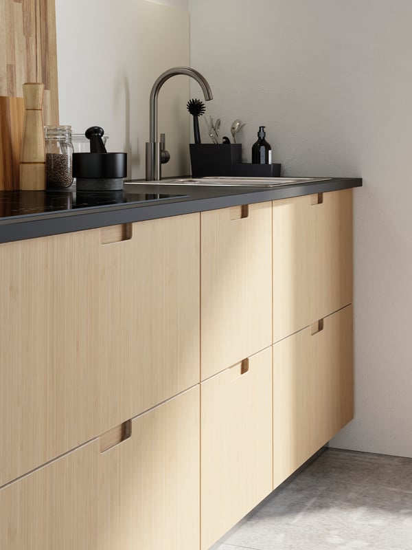 A kitchen with light bamboo drawer fronts, a matte anthracite countertop, a sink with a kitchen faucet.