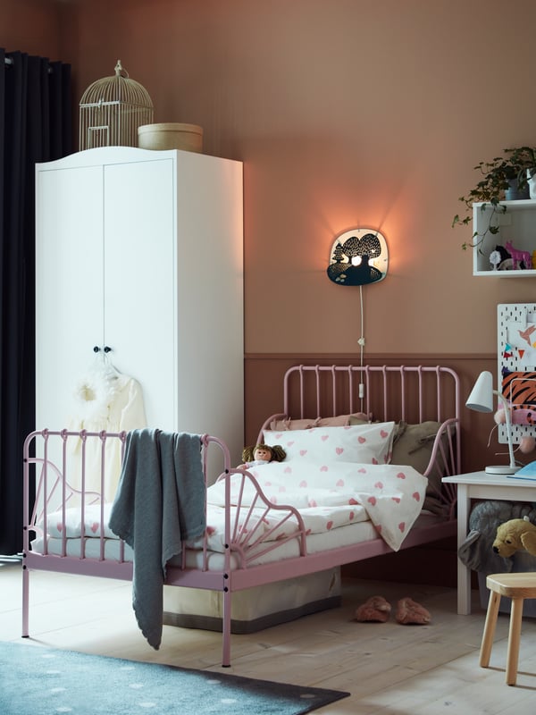 Una habitación infantil con un clóset blanco, una cama infantil extensible MINNEN color rosa con ropa de cama blanca y rosa.